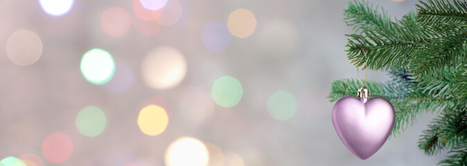 Christmas tree branch with heart-shaped ornament against blurred lights on grey background, bokeh...