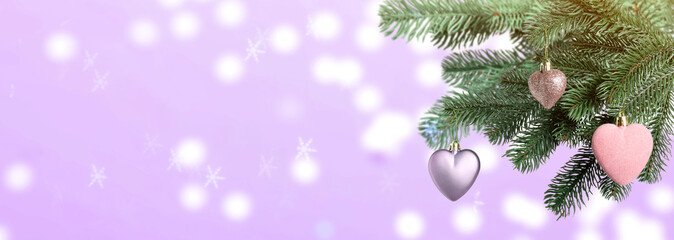 Christmas tree branches with heart-shaped balls against blurred lights on violet background, bokeh...