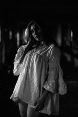 Naklejka premium Young woman with long hair wearing a white oversized shirt poses confidently in an abandoned building, showcasing a blend of elegance and urban decay in monochrome