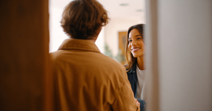 Young woman smiling warmly while greeting a man at the doorway in a cozy indoor setting, capturing a moment of friendly interaction and connection