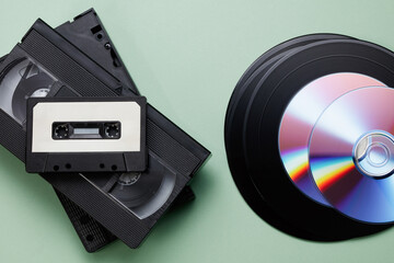 Obraz premium Texture of vintage retro vinyl records, retro acoustic, audio cassette tape, black video tape cassette, CD disc on a green background. Saving data, music, movies, videos. Top view. 