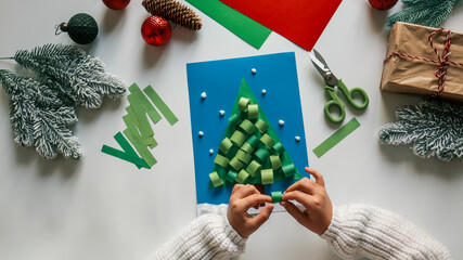 Child making a Christmas tree card with paper and decorations