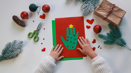 Child's Christmas handprint art with decorations and gifts on a white surface