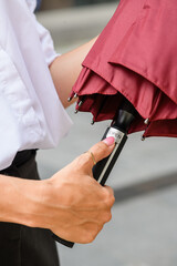 Woman pressing button to open red umbrella outdoors.
