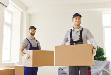 Portrait of a two positive man movers company handling boxes during relocation to new home or...