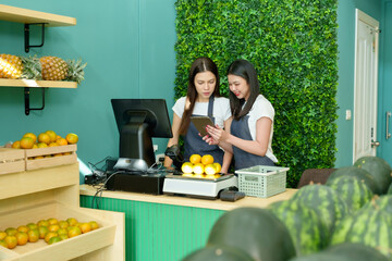 Asian lesbian couple working together inside small fruit store checking inventory on tablet showing collaboration and partnership in LGBTQ owned business with positive mood in modern shop