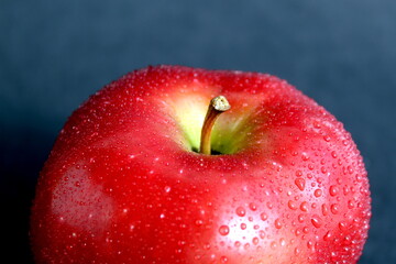 On a black background lies a whole red apple with splashes of water.	