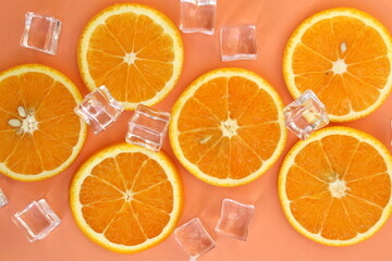 Sliced ​​oranges with ice cubes lie on a pink background.