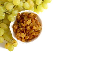 On a white background there is a white bowl with yellow raisins and fresh grapes.