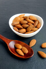  On a black background there is a wooden spoon and a bowl with almonds.