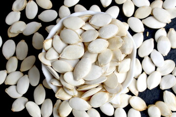 On a black background there is a bowl with unpeeled pumpkin seeds.