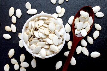 On a black background there is a bowl with a wooden spoon containing pumpkin seeds in their shells.