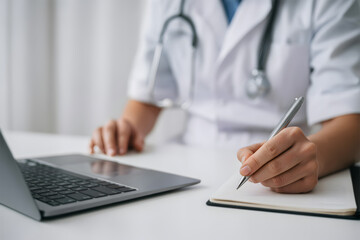 Doctor Hand Writing Medical Notes and Working on Laptop Healthcare Documentation Research