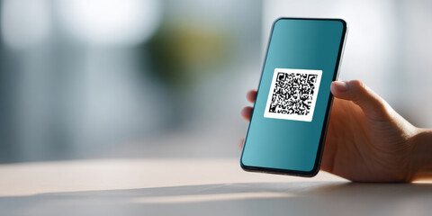Close-up of hand holding smartphone displaying QR code on screen with blurred background and soft lighting