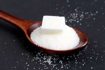 There is a wooden spoon with granulated sugar on a black background.	