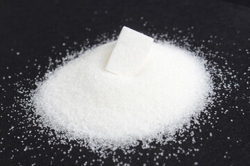 On a black background lies a small pile of sugar with one cube.	