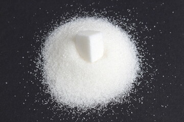 On a black background lies a small pile of sugar with one cube.