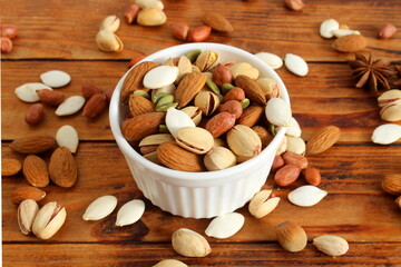 There is a plate with a pile of different nuts on the wooden table.	