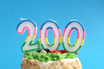 On a blue background there is a festive cake with an anniversary candle with the number 200.