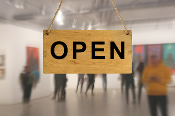 An "Open" sign against a blurred background of an interior with people