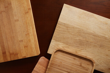 Overhead view of various wooden cutting boards and serving trays with different textures, including bamboo and natural wood grain, arranged randomly on a dark brown table surface.