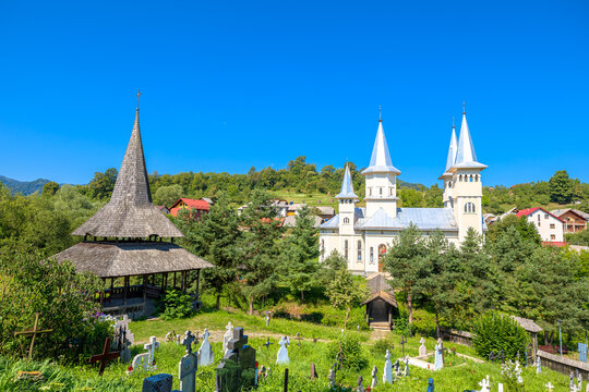 Saint Parascheva church, a historical wooden orthodox church, standing prominently on a sunny day next to an overgrown graveyard old tombstones and crosses in Poienile Izei, Maramures in Romania