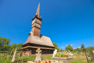 Ancient wooden Greek-Catholic church of Archangels Michael and Gabriel on a grassy hill in rural surdesti in Maramures, Romania