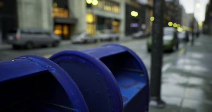 Vibrant blue mailboxes stand proudly on a city street, illuminated by soft evening lights. Cars pass by as pedestrians stroll, creating a serene urban atmosphere.