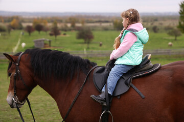 Obraz premium Equine assisted therapy. Little girl riding beautiful horse outdoors. Lovely domesticated pet
