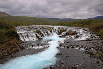 Turquoise water flowing over the stunning Brúarfoss waterfall in Iceland, long exposure, surrounded by rugged volcanic landscape and natural beauty