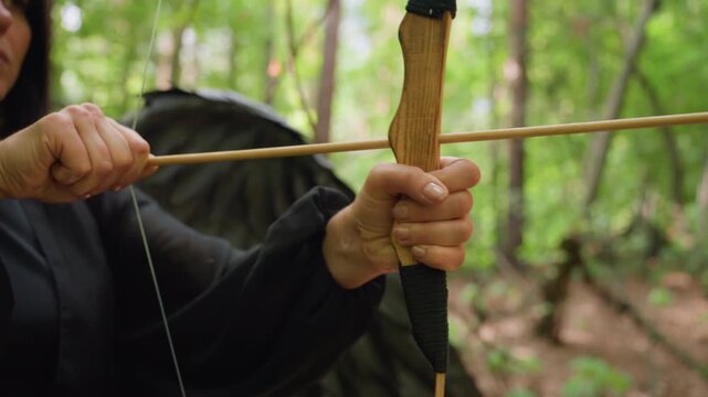 Close up of archer hands pulling wooden bowstring and aiming arrow in forest, sunlight reflecting on natural wood texture, showing focus, strength, and precision in calm mystical atmosphere