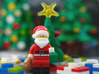 Obraz premium Tambov, Russian Federation - October 23, 2025 A Lego Santa Claus minifigure with a sack of presents standing in front of a Christmas tree and surrounded by gifts.