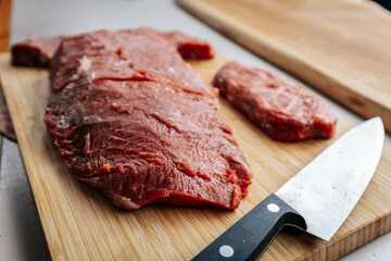 Close-up of neatly sliced raw beef on a wooden cutting board, showcasing the vibrant red color and fine marbling, ready for seasoning or cooking.