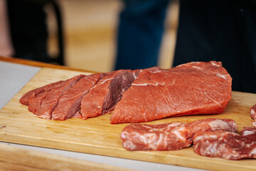 Close-up of neatly sliced raw beef on a wooden cutting board, showcasing the vibrant red color and fine marbling, ready for seasoning or cooking.
