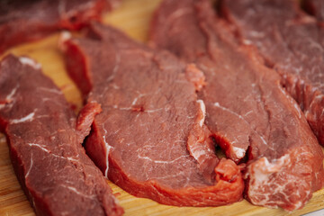 Close-up of raw beef steaks seasoned with salt and pepper, laid out on a wooden cutting board, ready for grilling at an outdoor cooking event.