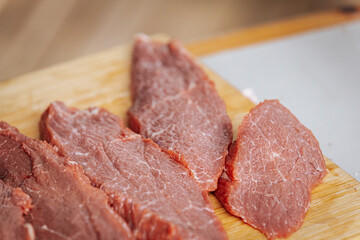 Close-up of raw beef steaks seasoned with salt and pepper, laid out on a wooden cutting board, ready for grilling at an outdoor cooking event.