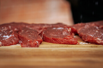 Close-up of raw beef steaks seasoned with salt and pepper, laid out on a wooden cutting board, ready for grilling at an outdoor cooking event.