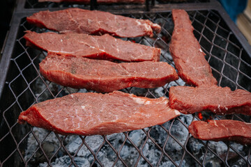 Close-up of raw beef steaks sizzling on a grill over hot coals, with visible seasoning and sear marks beginning to form.