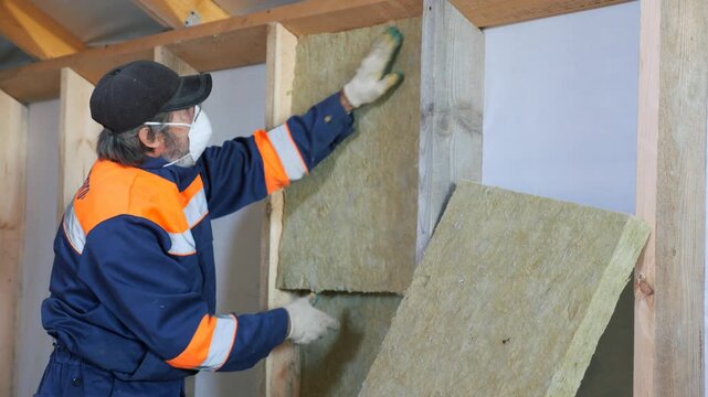 Insulation of a frame house with mineral wool. Cutting, fitting, laying insulation. Construction works.