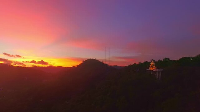 Aerial view of Sunset above Khao Rang viewpoint. view of a town nestled among lush green mountains at sunset, with a Pavilion structure perched on the hillside at Phuket town at Dusk