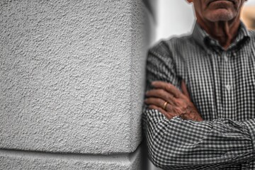 Quiet Contemplation: An senior man leaning against a stone structure, his expression reflects thoughtful introspection. His arms crossed in a moment of quiet reflection.