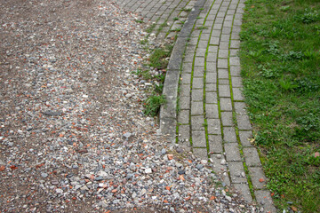 Textured gravel pathway transitions into a curved brick sidewalk, surrounded by lush green grass, showcasing the contrast between natural and man-made elements