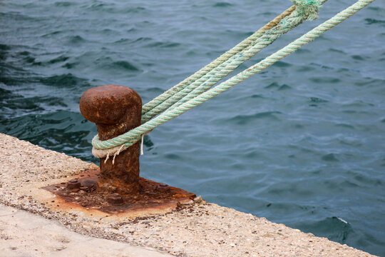 Rusty mooring bollard with tied ship rope in the port