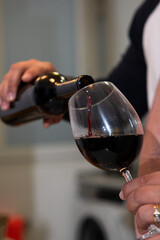 Hand pouring red wine from a bottle into a glass
