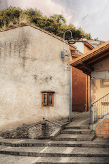 Rustic narrow street corner in Cudillero, Spain, with textured stucco walls, old wooden window, stone steps and vintage lamp under warm soft light creating a cozy village atmosphere