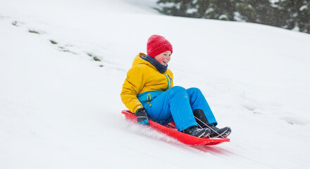 Child sledding down snowy hill wearing bright winter clothes