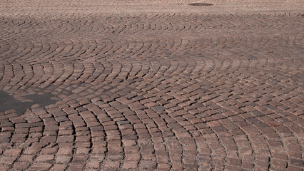 Old market square pavement made of natural stone blocks arranged in curved patterns. 