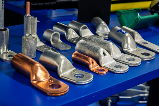 A selection of various electrical cable lugs and terminals, in copper and silver-colored metals, displayed on a blue surface. Essential components for robust electrical connections in industrial and p