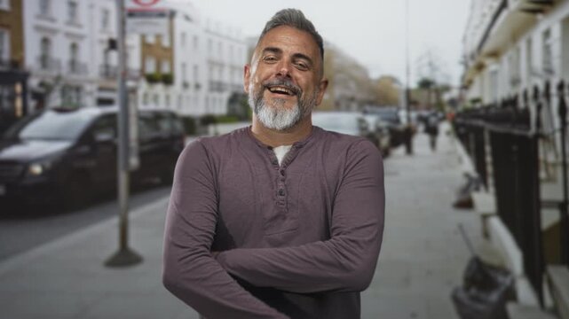 Middle aged man with hand to forehead smiling on city street, beard visible and arms sometimes crossed; maturity confidence joy.