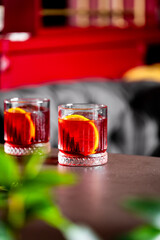  vibrant red cocktail with an orange slice in a fluted glass, set on a dark wooden table with a soft-focus background.